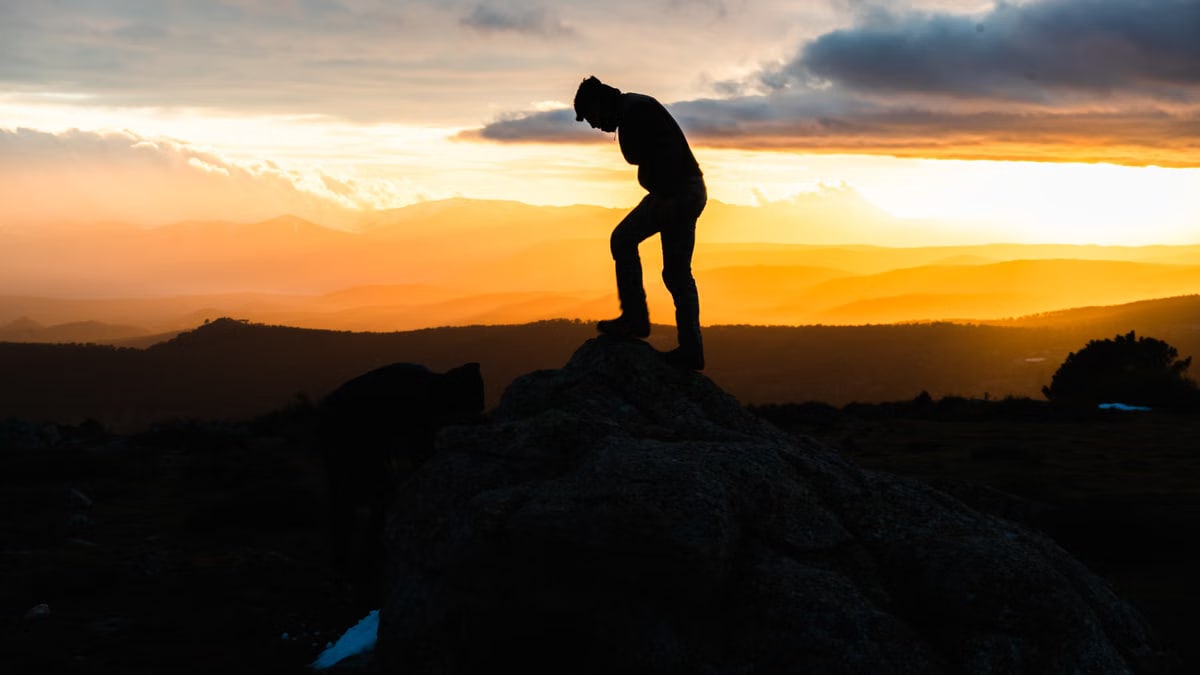 A silhouette of a person on a rock, set against a stunning vibrant sunset with dramatic clouds.